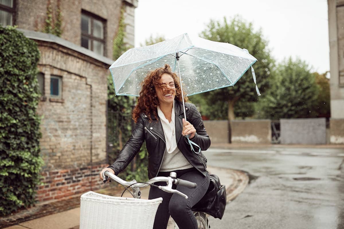 A woman with an umbrella smiles as she rides a bicycle.