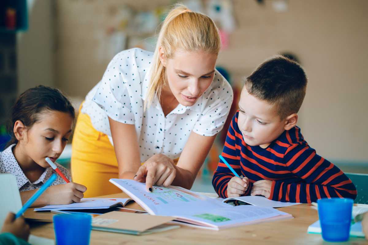 Female school teacher works with young students in classroom