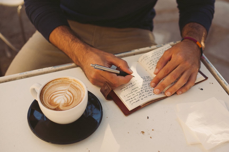 Worker writing in notebook with coffee