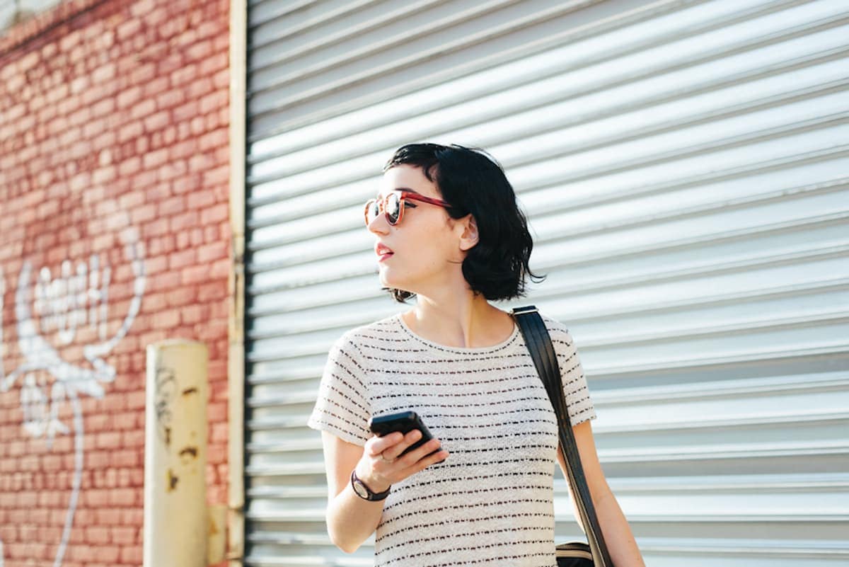 young woman walking outdoors with cell phone in her hand