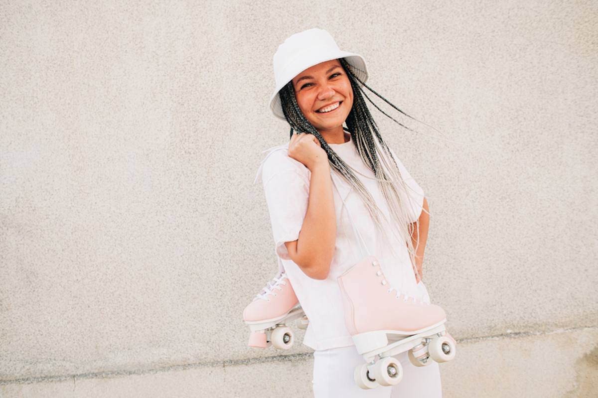 Smiling woman in white with pink roller skates slung over her shoulder