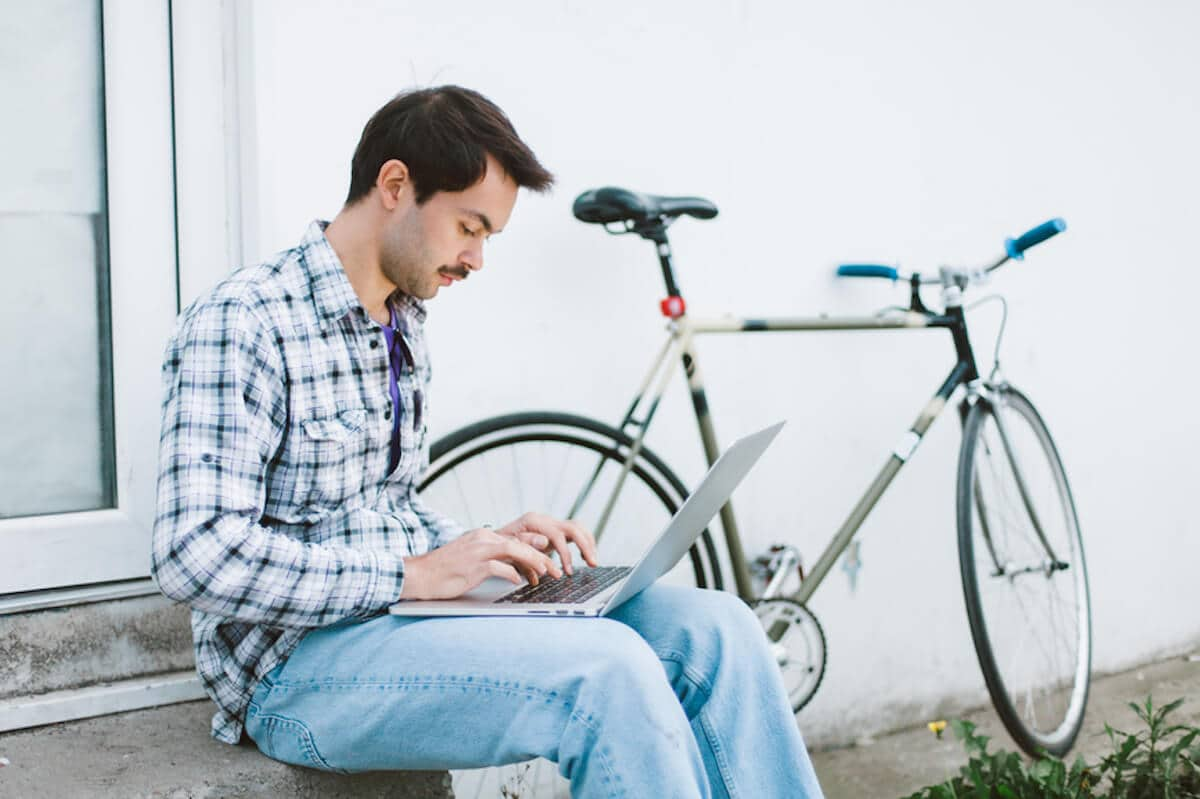 A man sitting outside types on his laptop computer