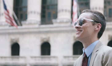 Business professional in suit with sunglasses on while looking up.