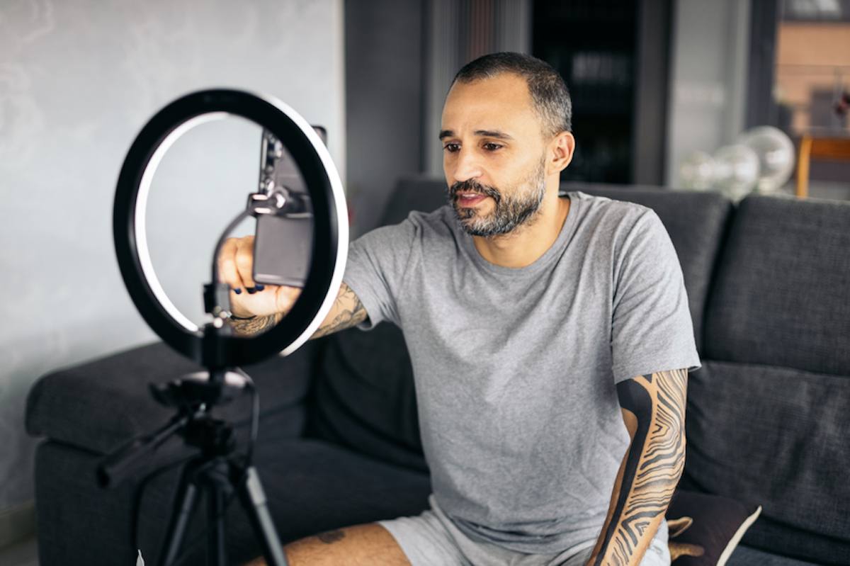 A social media influencer with short hair and a beard records a video at home