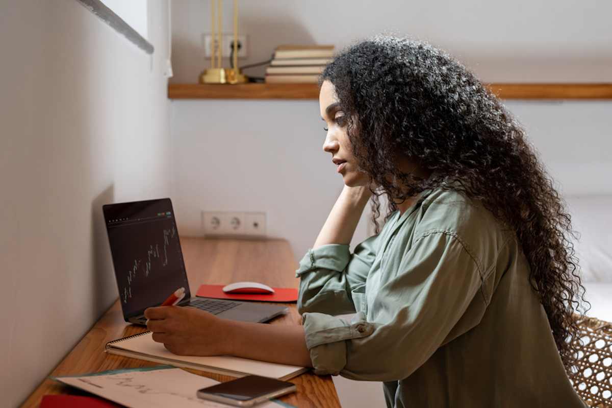 Una mujer con cabello rizado analiza la información bursátil en la pantalla de su computadora portátil