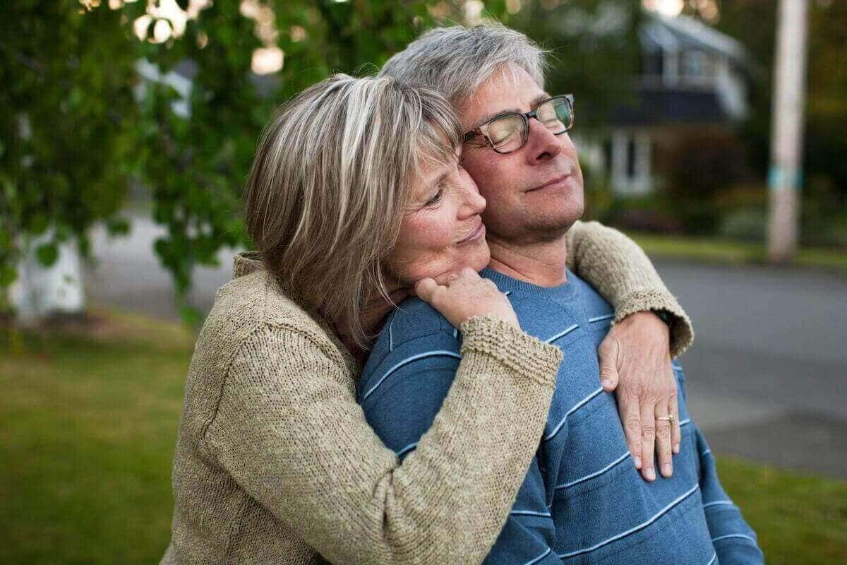 An older man leans back into the arms of his wife. 