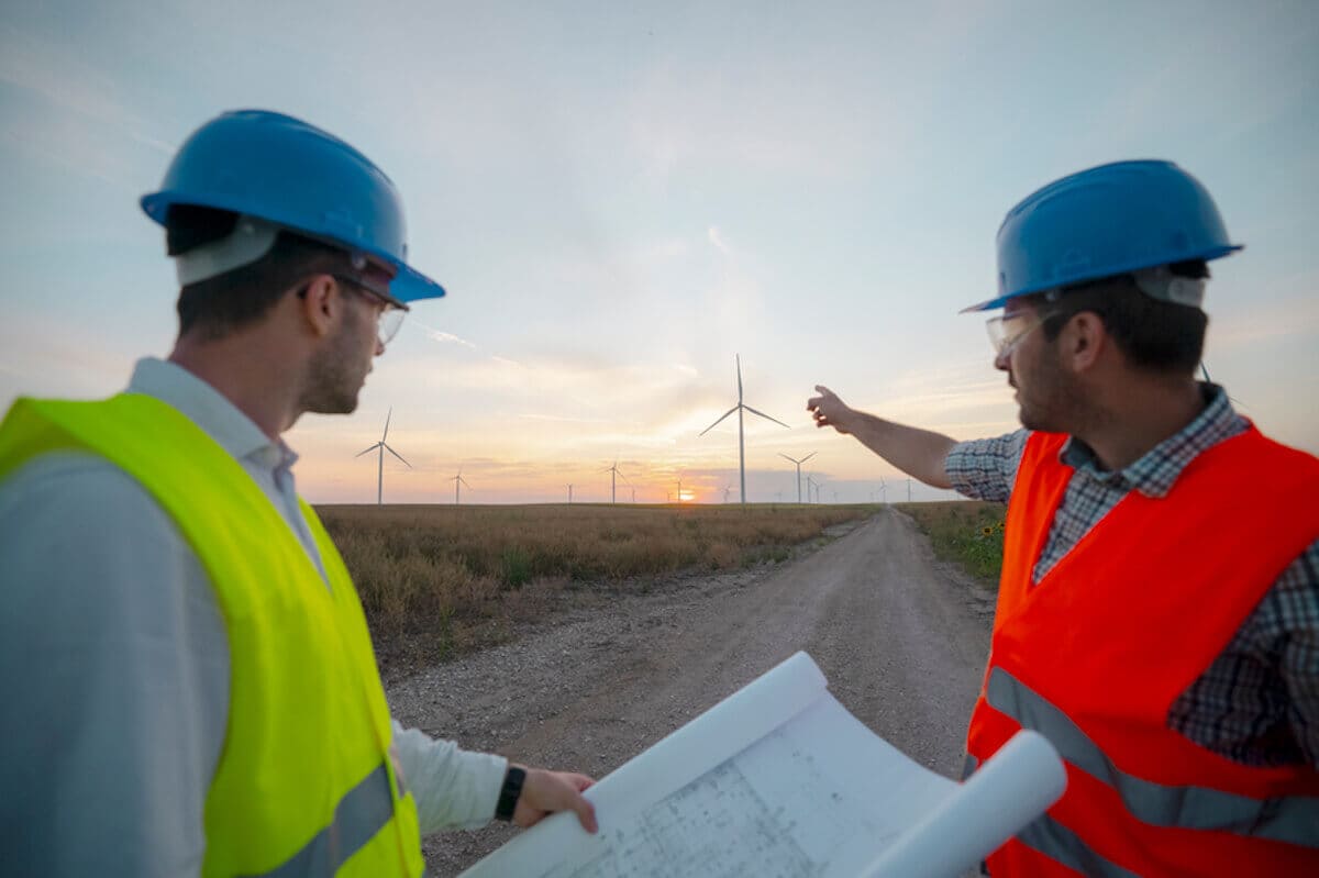 Two renewable energy technicians look out over a wind farm as they talk.