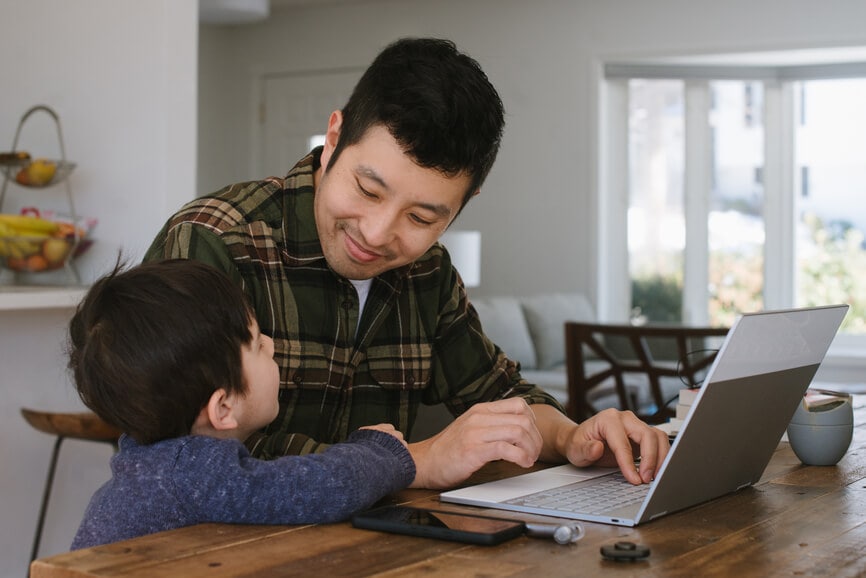 一个男人一边用笔记本电脑工作，一边对着他的孩子微笑。