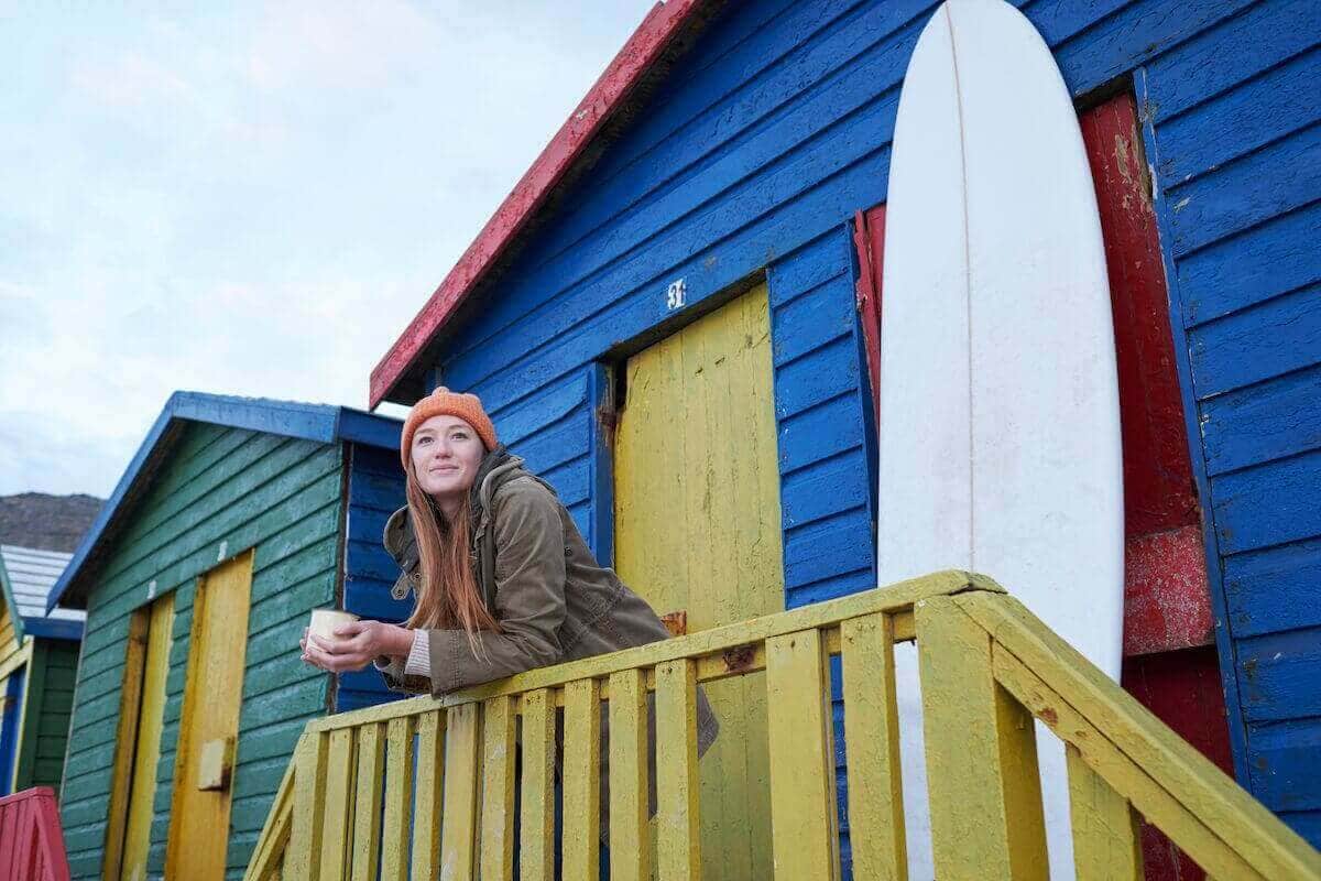 A young woman stands in front of a row of colorful beach houses.