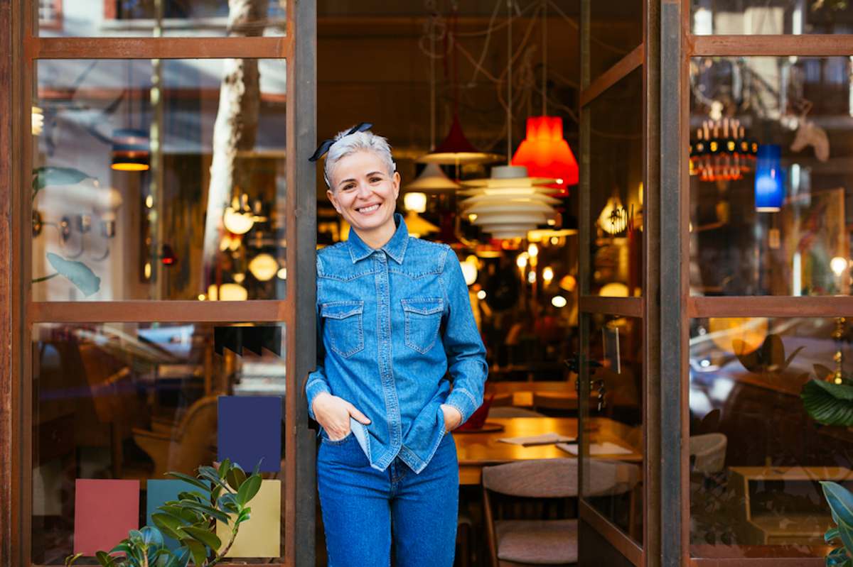 Smiling business owner stands in the doorway of her vintage furniture store