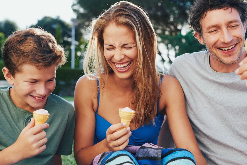 Family laughing and eating ice cream together on a hot summer day.