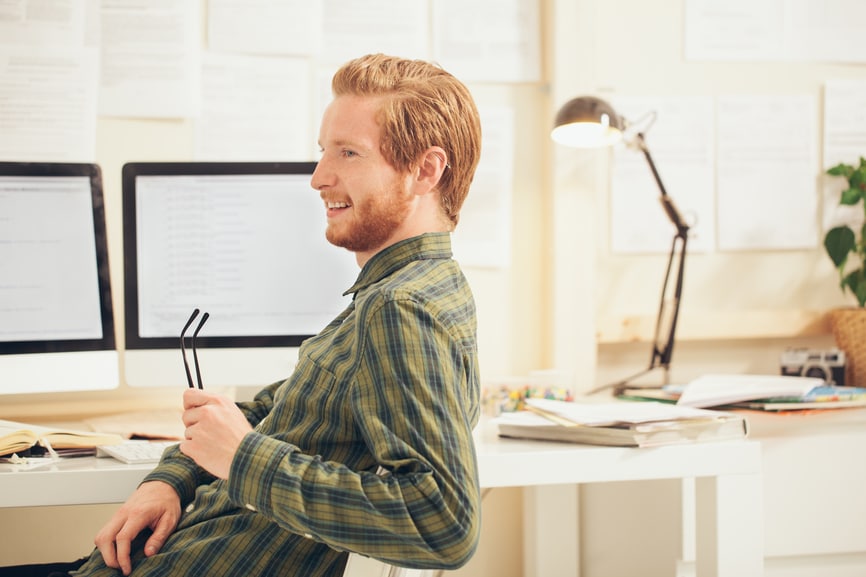 Male student smiling at his brightly lit desk area.