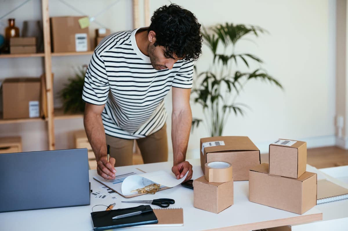 A man checks delivery papers while surrounded by packages.