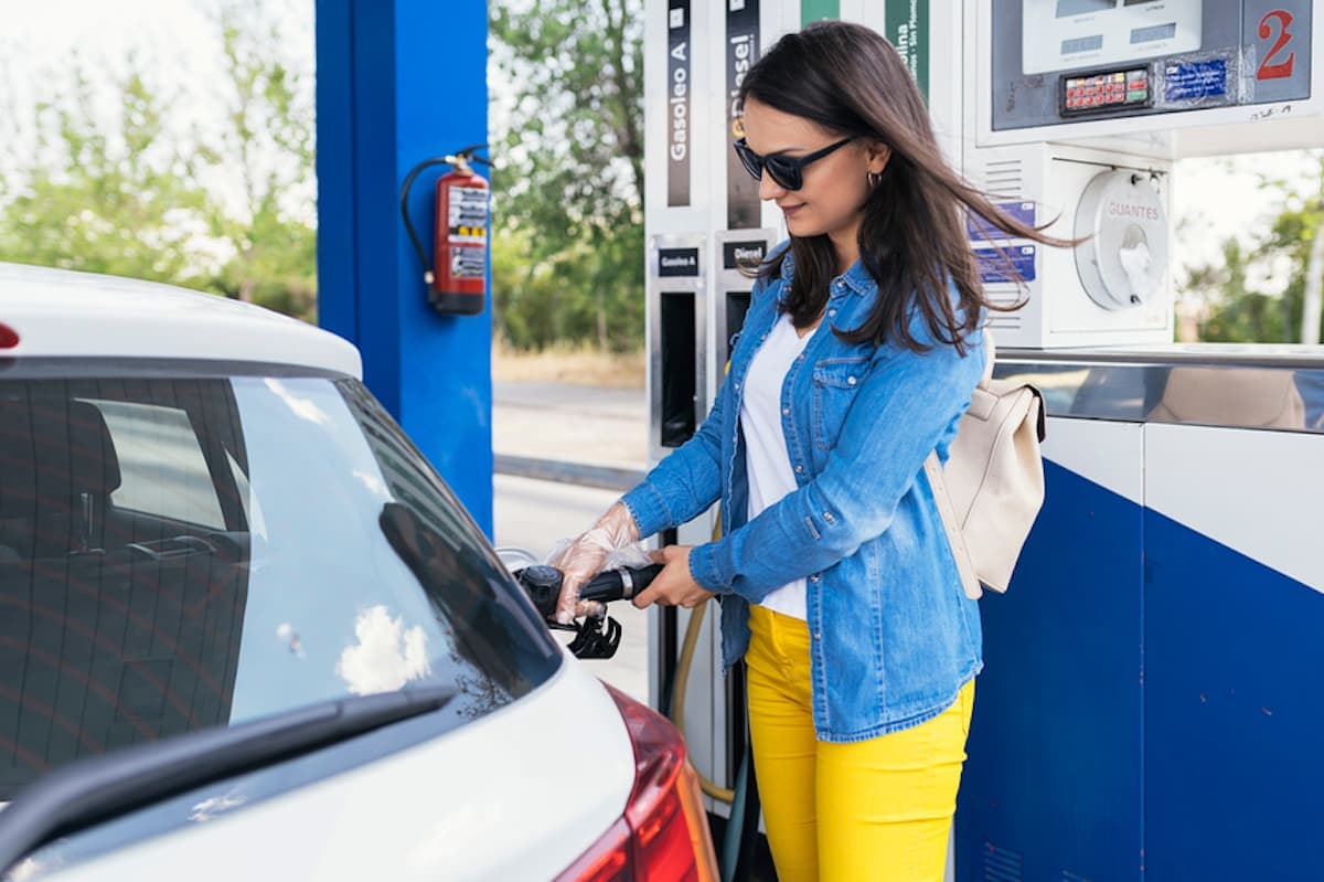 A young woman pumps gas into her car.