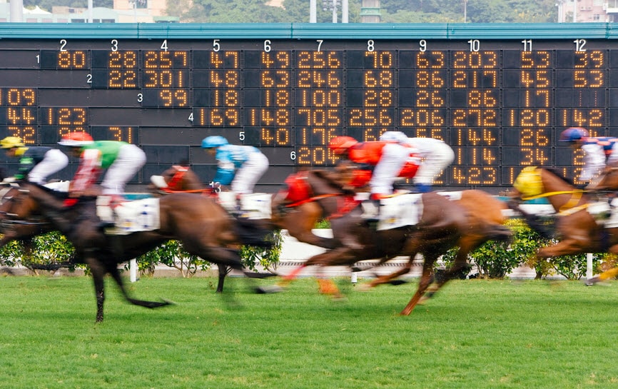Horses race past a large scoreboard