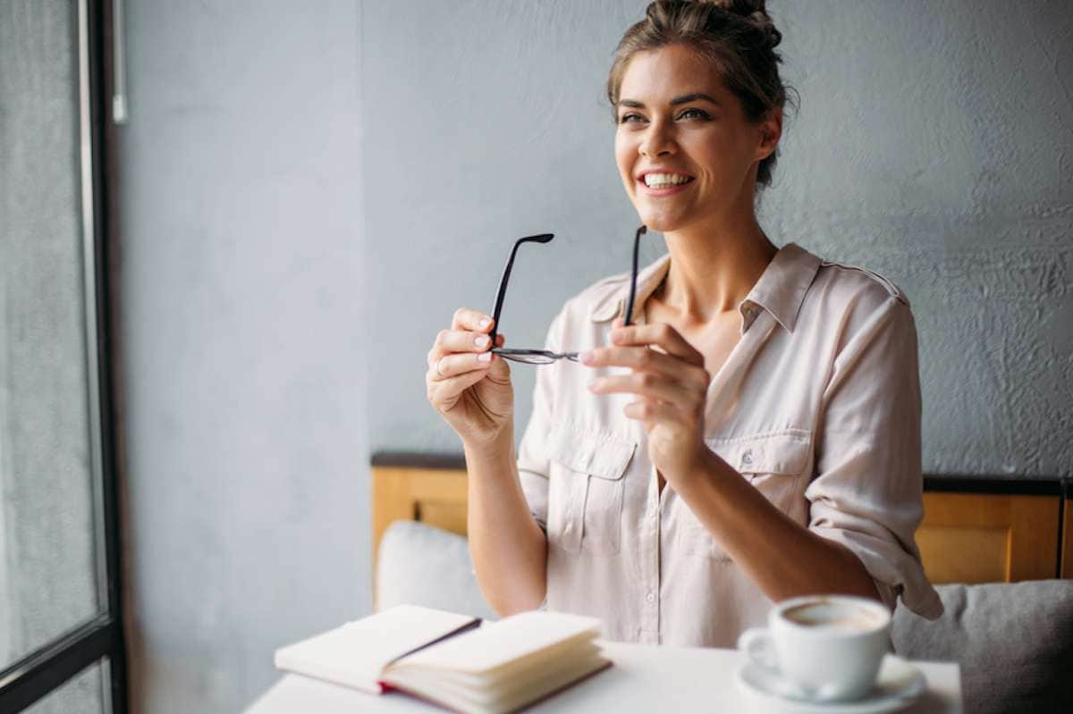 Smiling woman puts on her glasses in a coffee shop