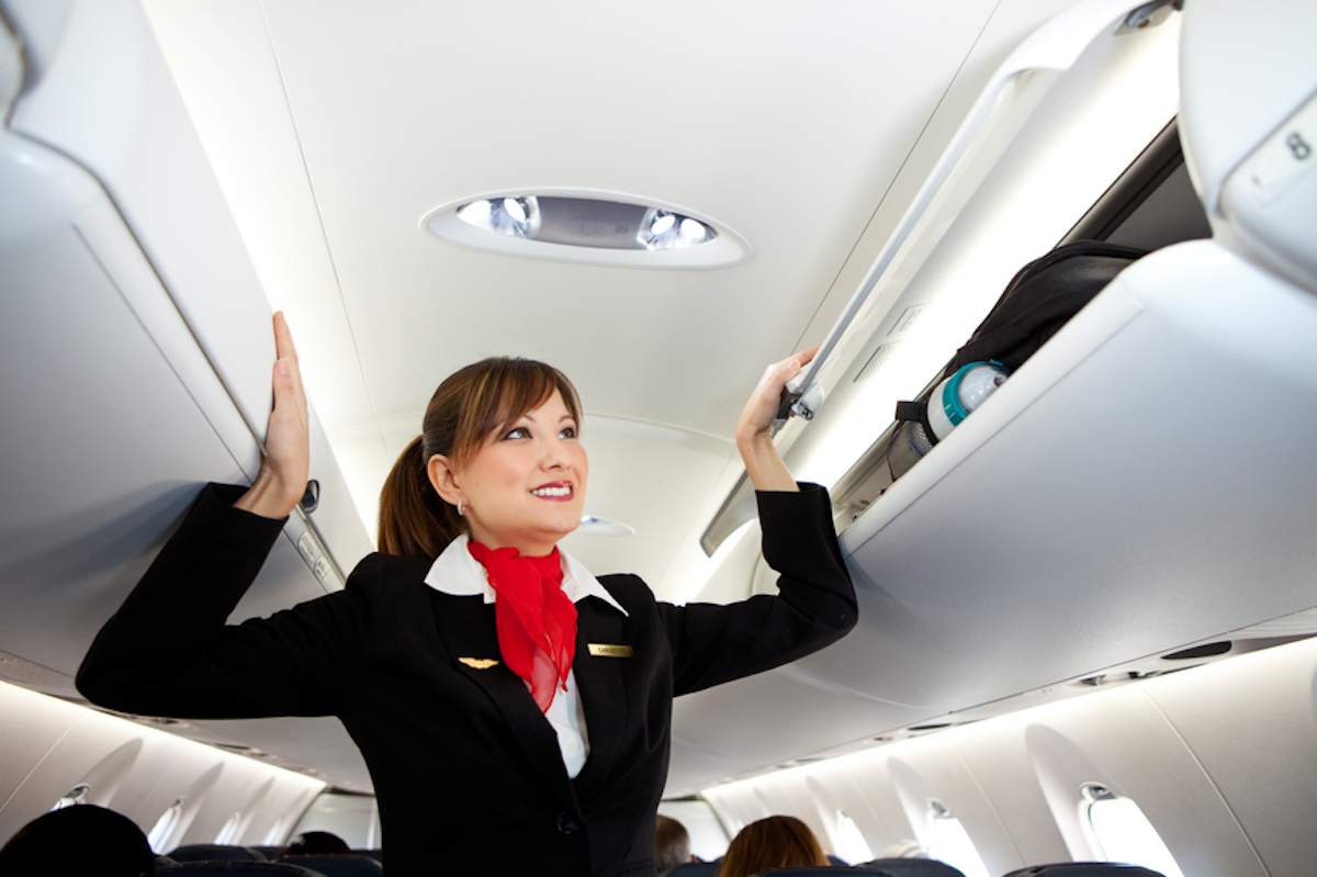 Smiling flight attendant closes compartments before take off