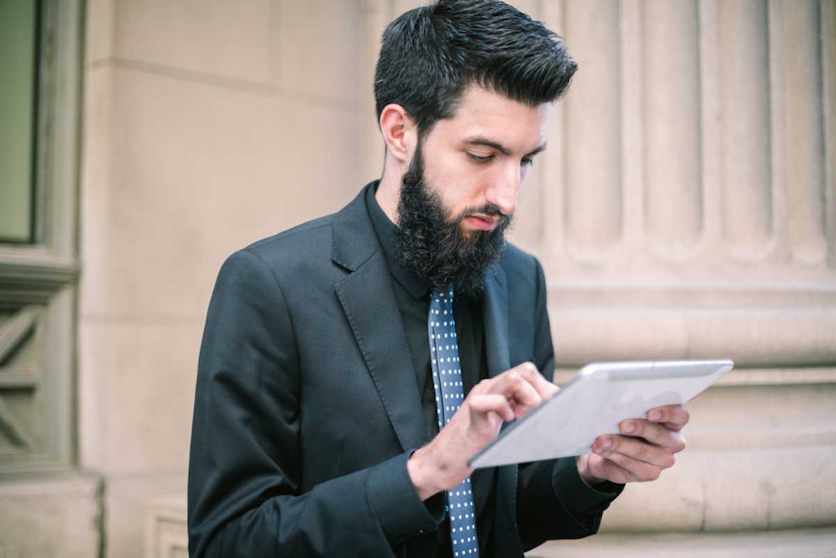 在金融区，一名穿着西装、留着胡子的年轻商人正在使用平板电脑