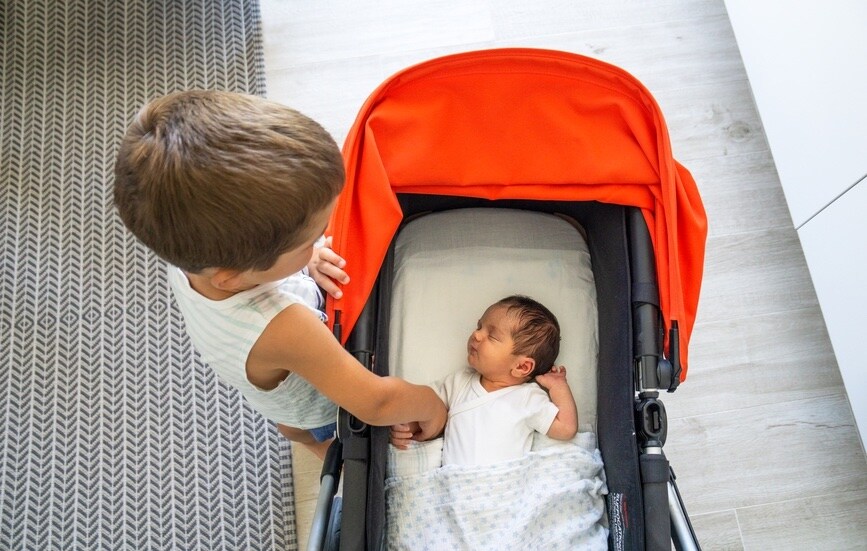 A young child looking over a baby in a stroller.