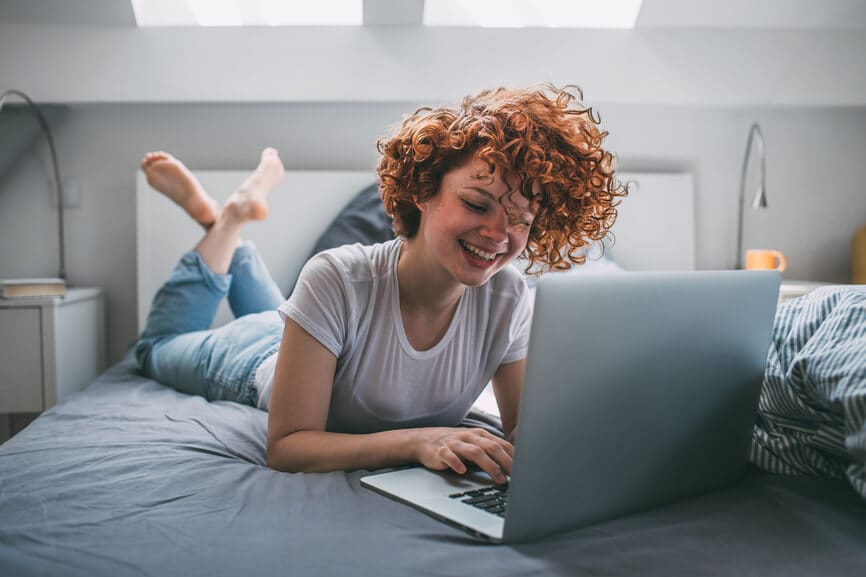 smiling woman on a bed using a laptop computer