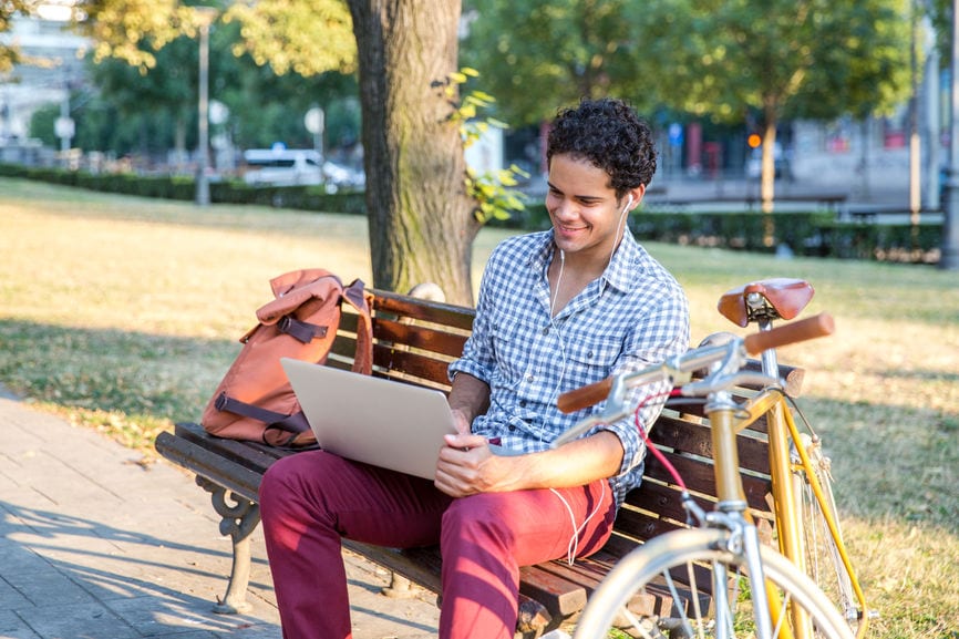 研究在公园长椅的一台膝上型计算机的男学生
