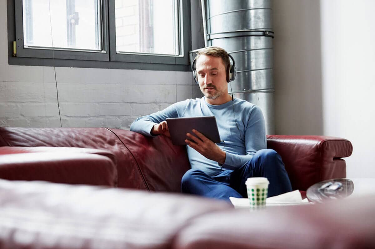 Businessman with headphones uses digital tablet on sofa at office