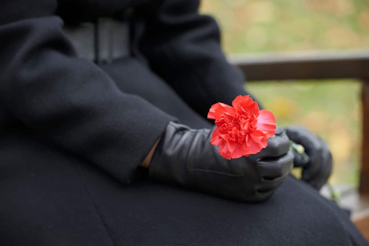 Female mourner holds single red flower