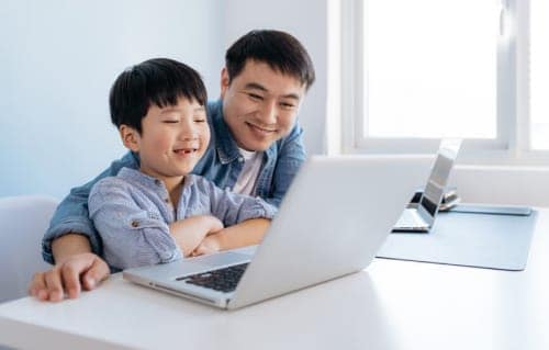 Father and son looking at computer together while smiling.