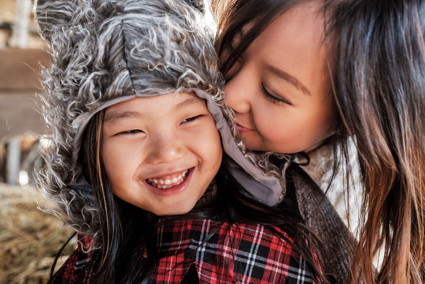 Mother kissing her smiling young daughter during fall season.