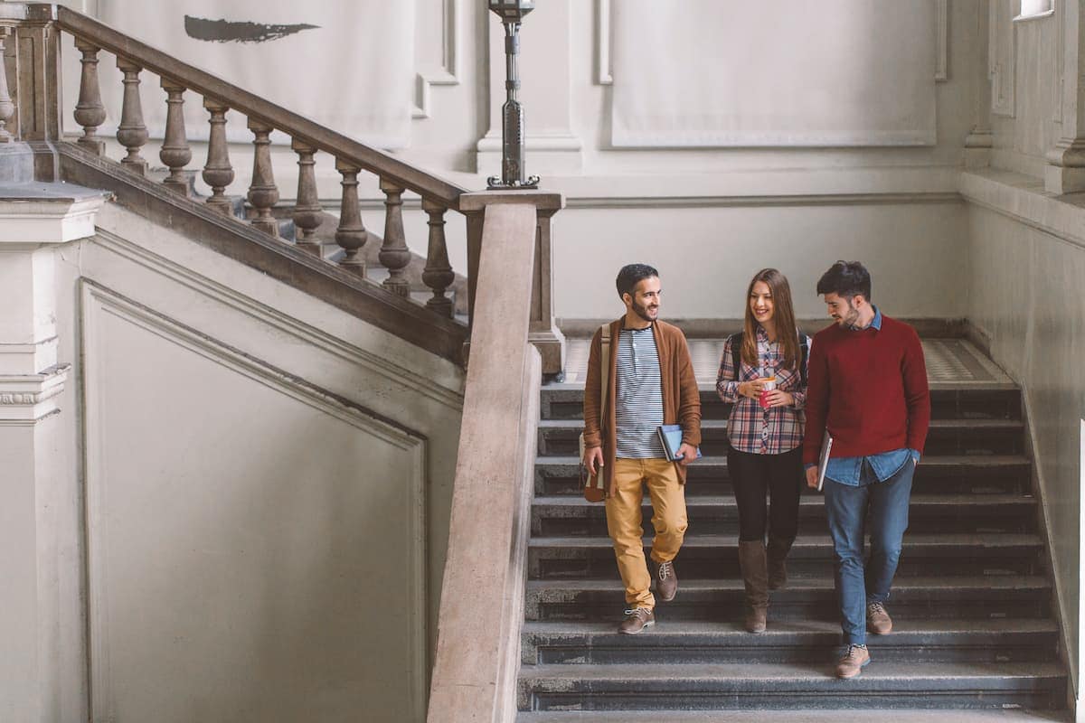 Un trío de estudiantes universitarios charlan mientras bajan unas escaleras.