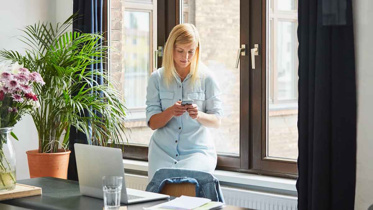 woman checking her mobile phone in front of office windows
