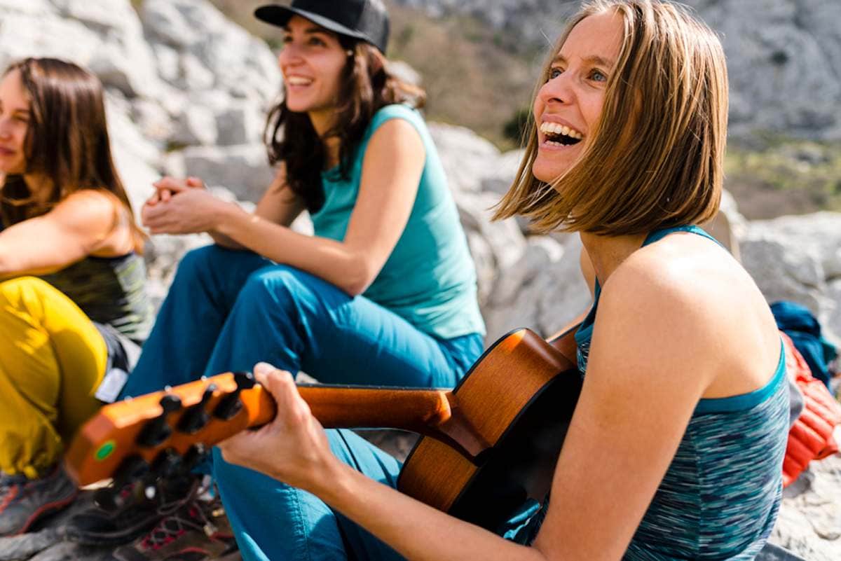 Group of female campers laughing and playing guitar