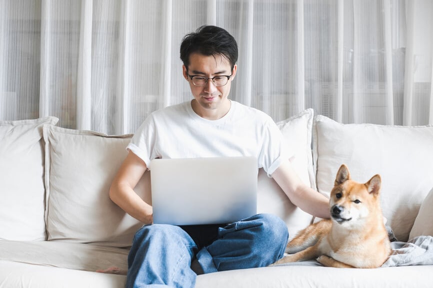man working on his laptop on the couch with his dog
