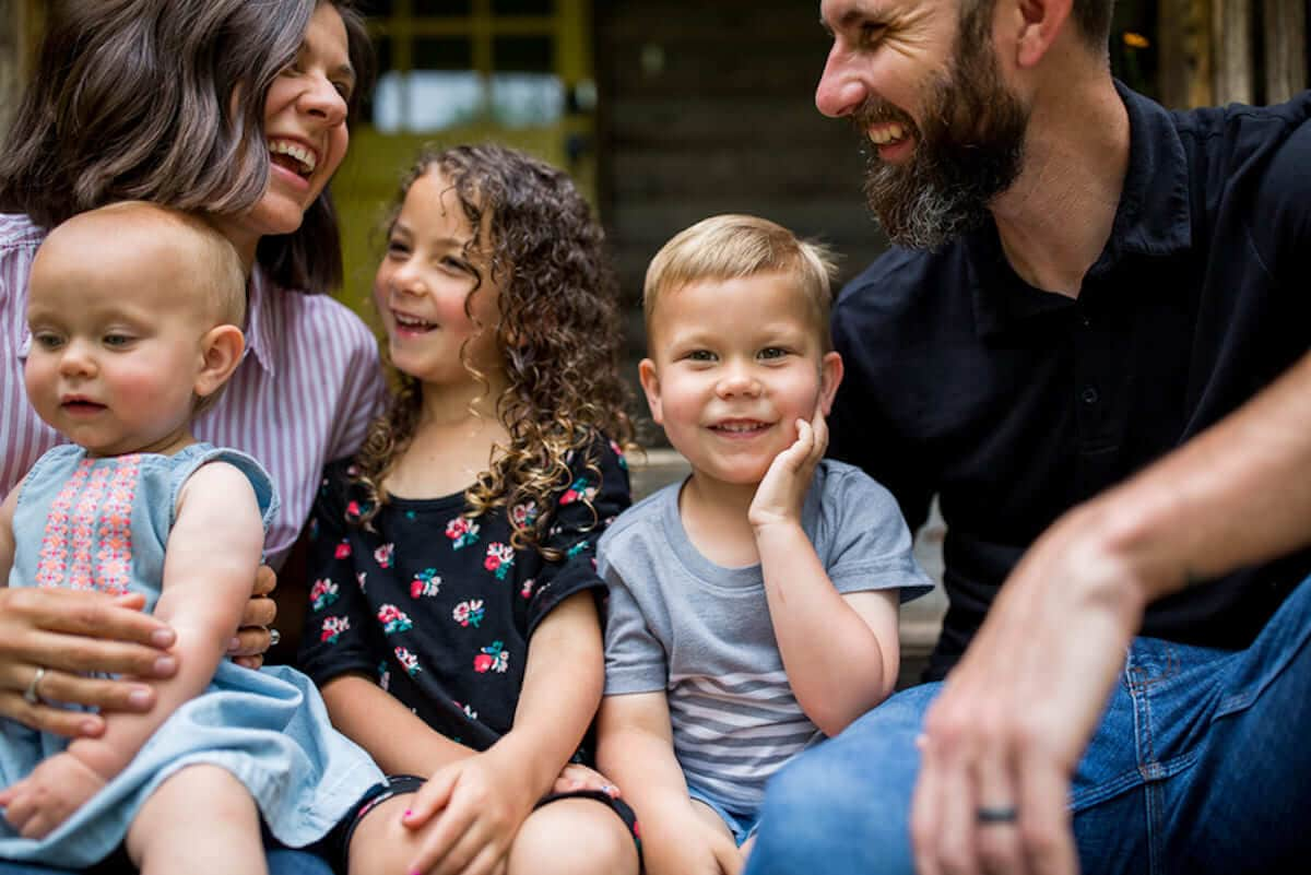 Parents with their young children sit on a porch and laugh