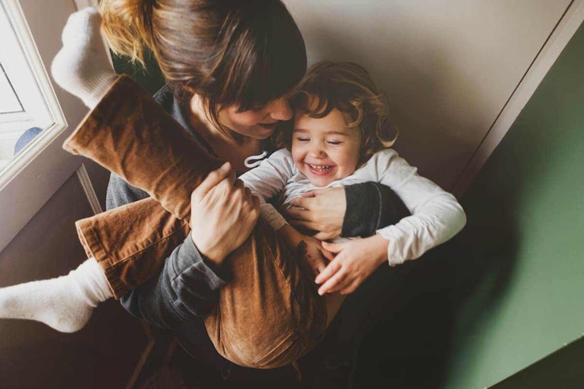 Young mom cuddling with laughing toddler girl