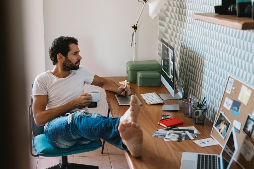 Man dressed casually, feet up on desk, working on laptop