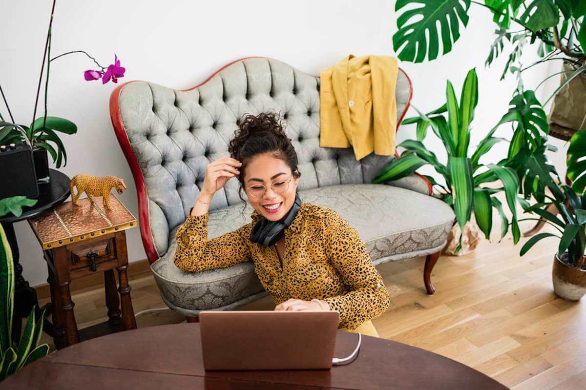 A female freelancer seated on the floor in front of a couch works on her laptop.