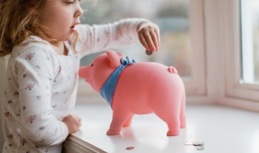 Child putting coins in piggy bank.