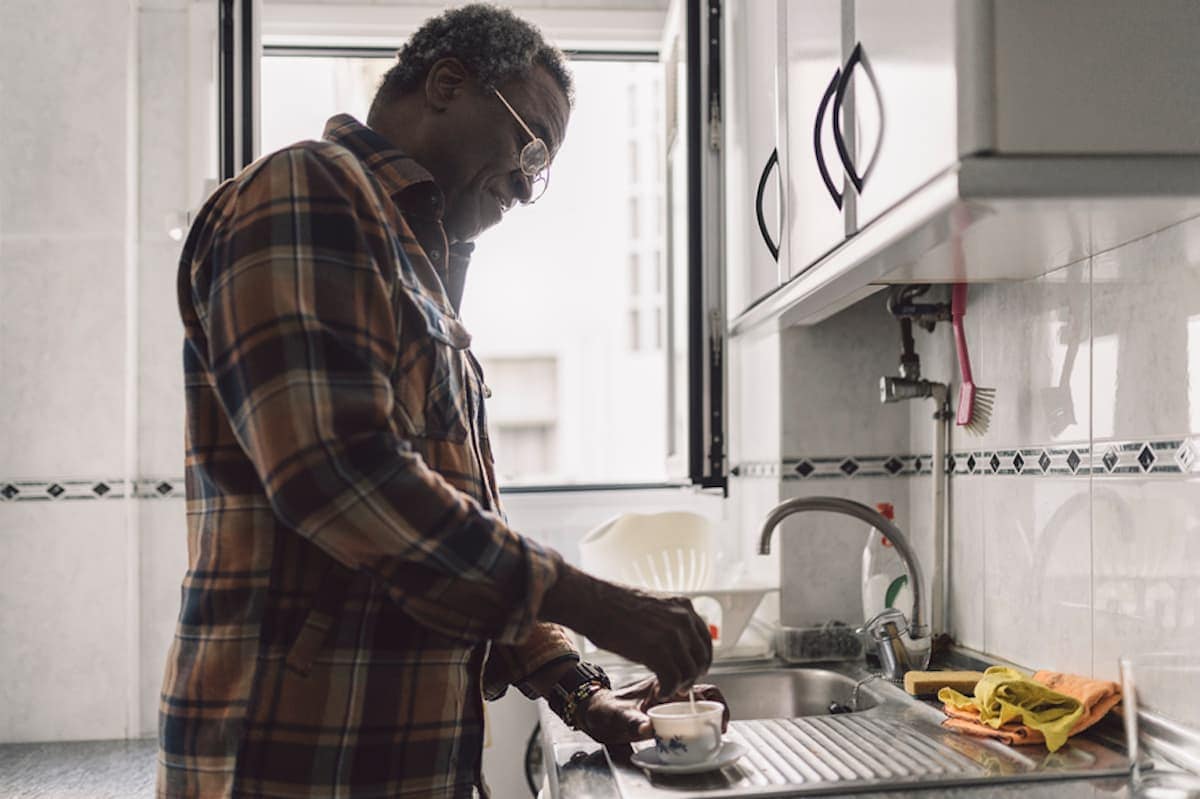 A retired Black man makes a cup of coffee at his kitchen counter.