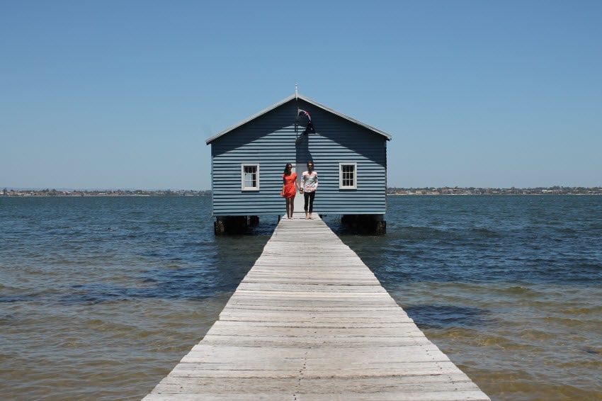 House on the water with a long dock and a couple holding hands in the distance