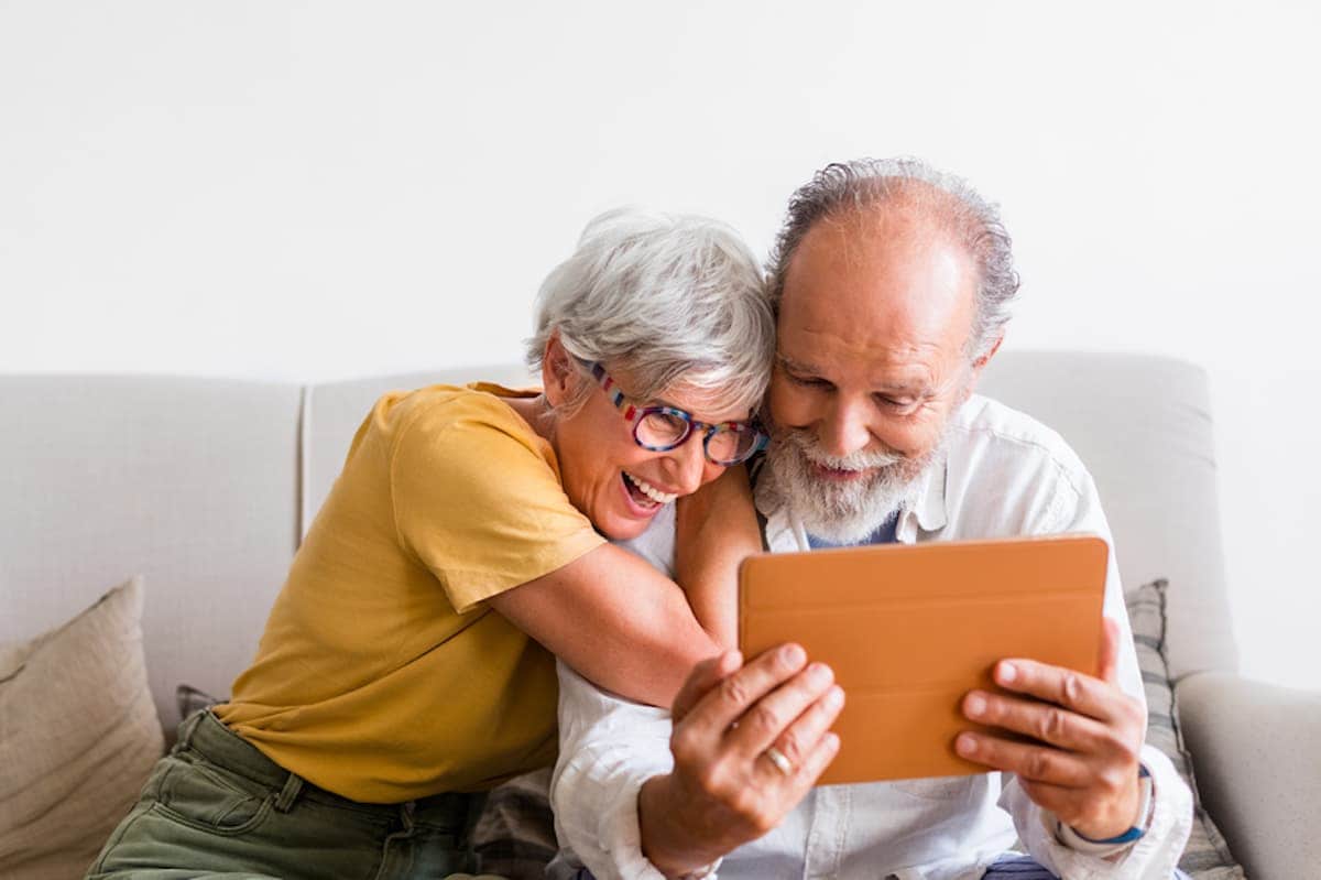 A senior couple hugs and laughs while looking at a tablet.