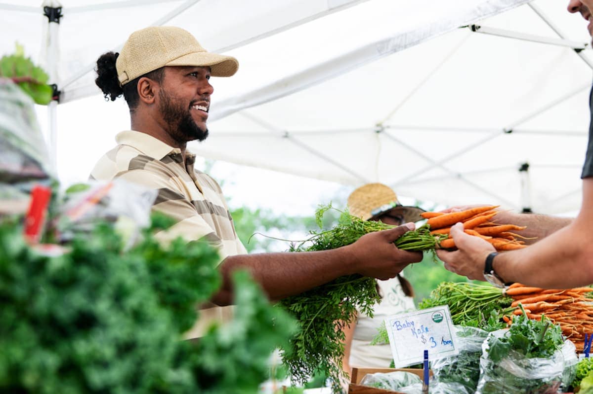 A Black farmer helps customers at his farmers market stand.