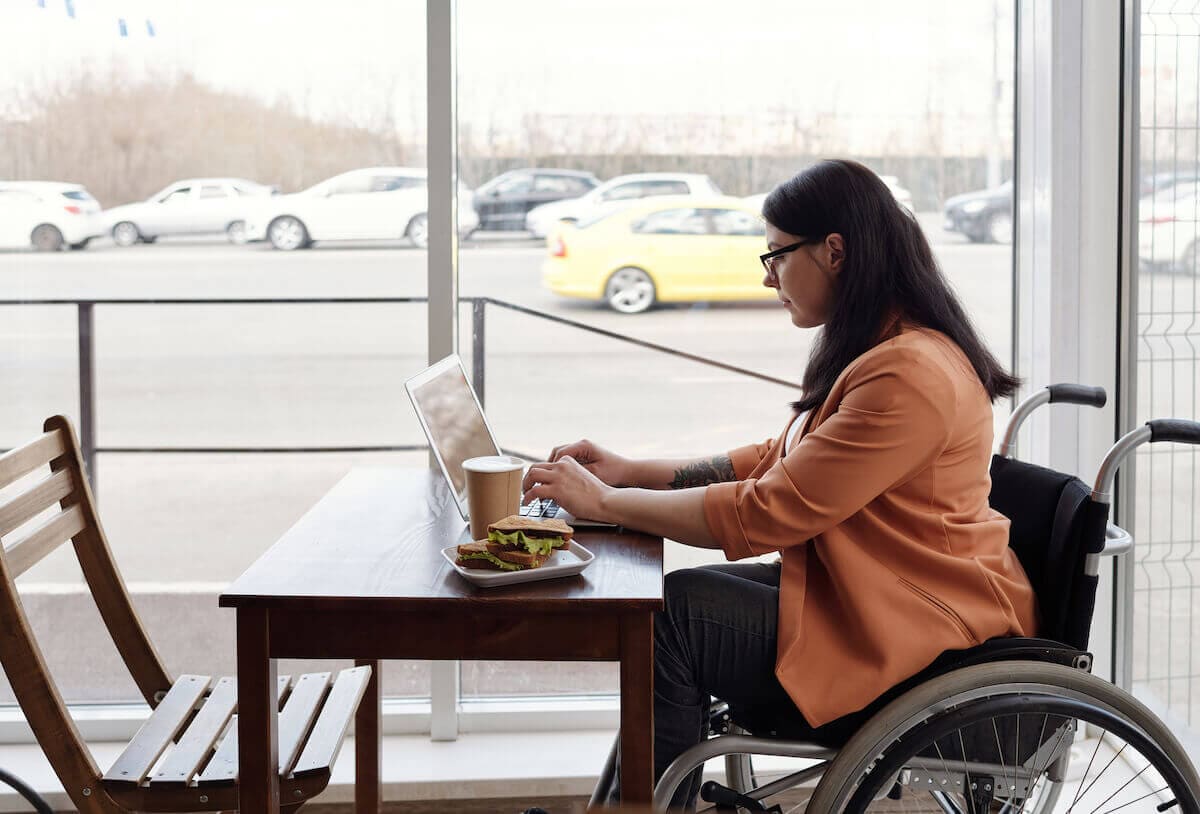 A woman in a wheelchair works on her laptop in a coffeeshop.
