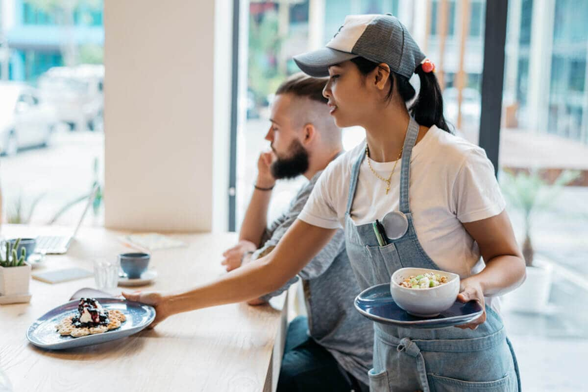 A woman working as a server sets a plate of food onto a counter.