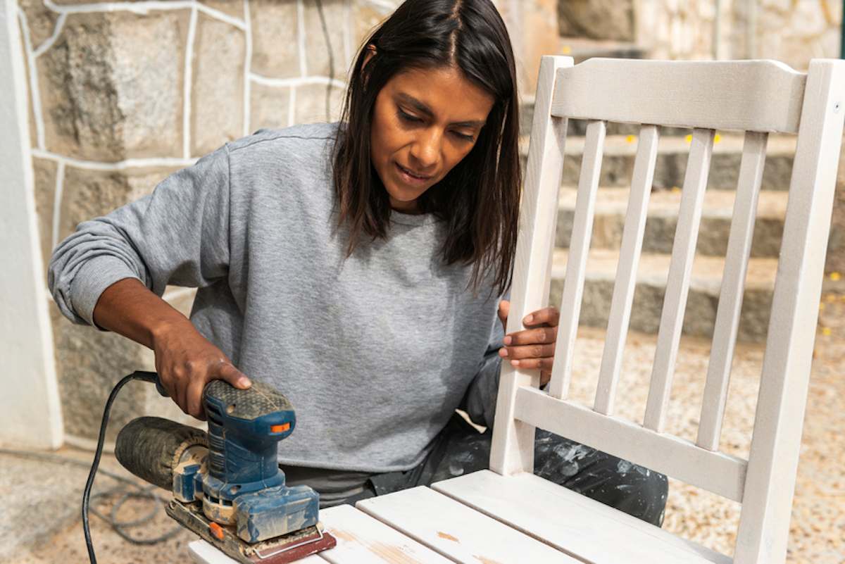 Una mujer usa una lijadora para restaurar una silla afuera