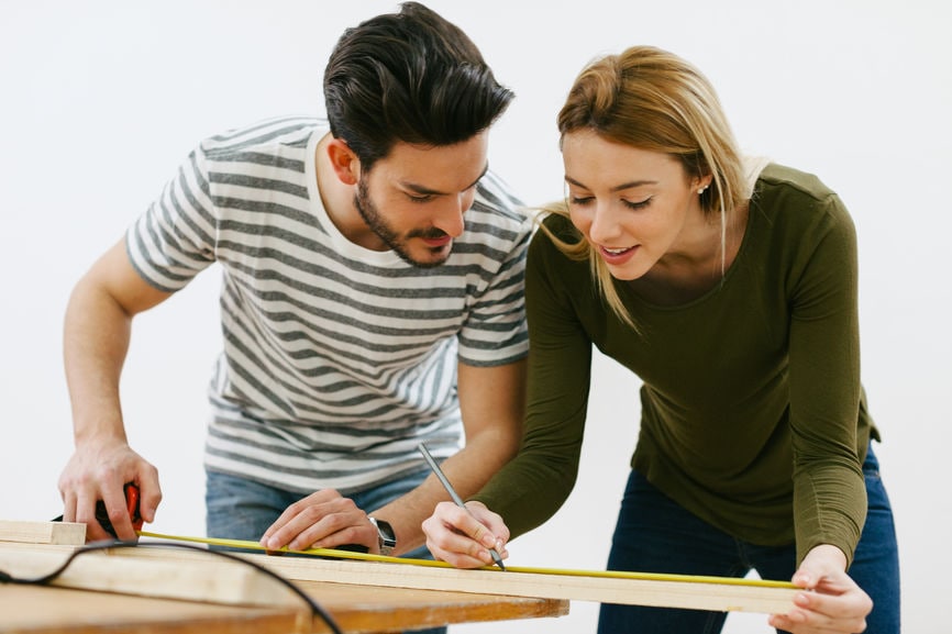 Young Couple Using A Tape Measure On A Wood Plank.