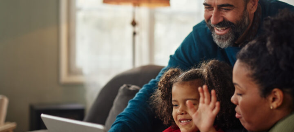 A man, woman, and a young girl smiling and waving in their living room