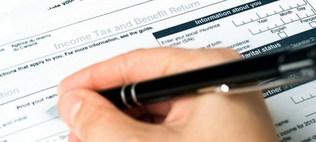 Closeup of a hand and pen filling out a paper income tax and benefit return form