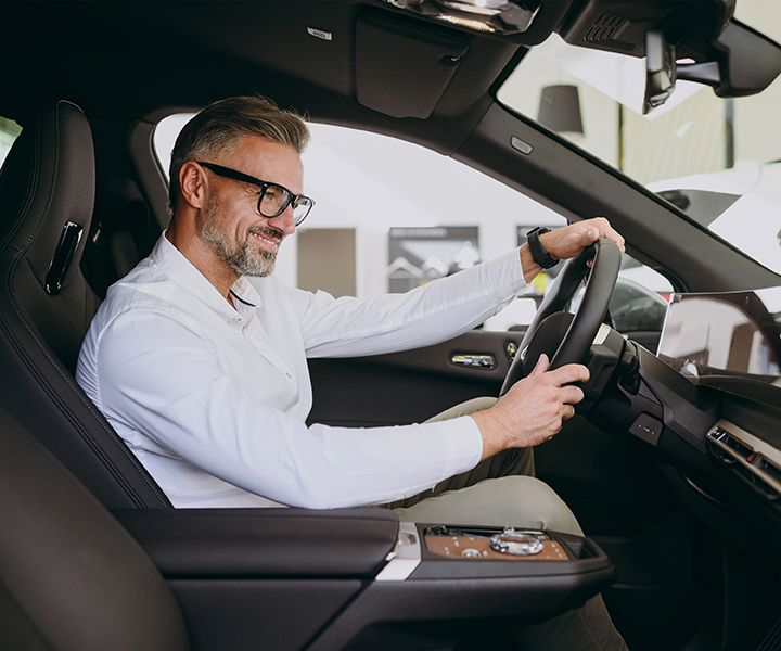 A person driving a car with a dog in the driver seat.