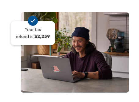 A young man smiling while working on his laptop in his home setting. Secondary illustration with “Your tax refund is $2,259” text and checkmark.